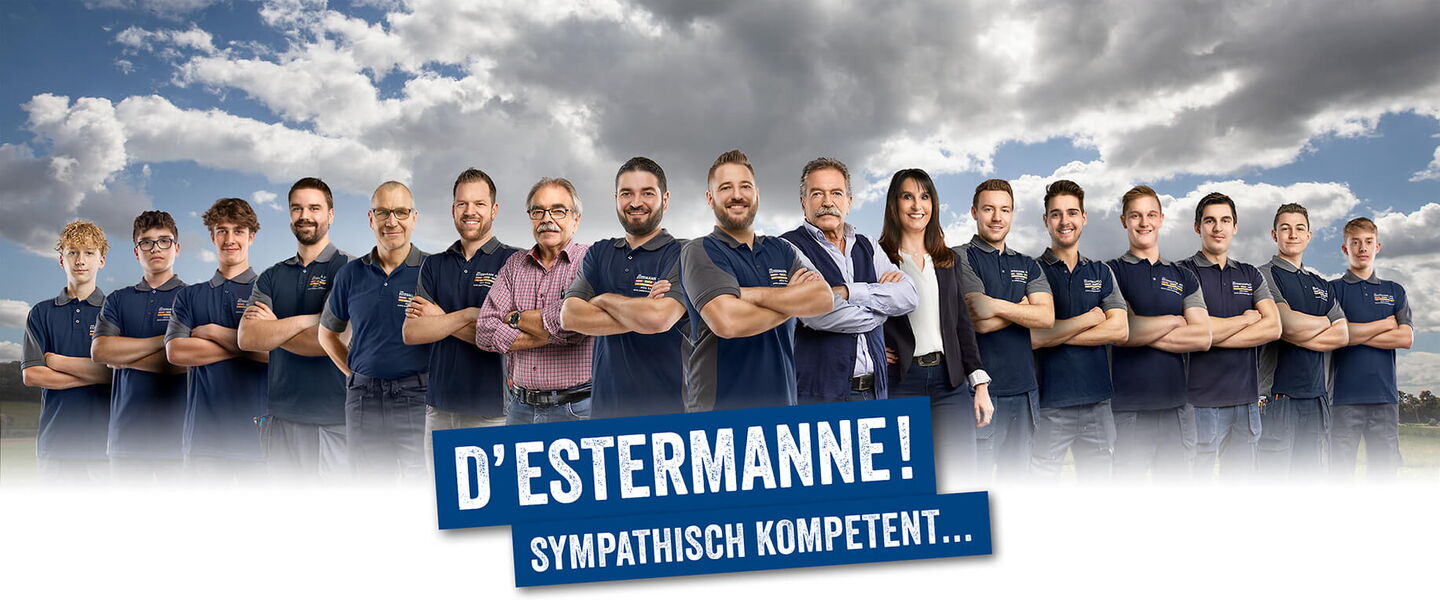 15 Handwerker und eine Frau formiert vor Wiese und Wolkenhimmel