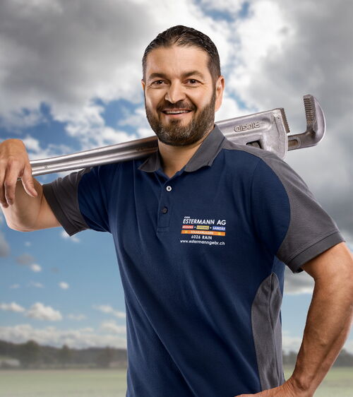 Handwerker mit blauem Shirt und grosser Rohrzange vor Wiese und Wolkenhimmel