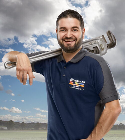 Lars Estermann Handwerker mit blauem Shirt und grosser Rohrzange vor Wiese und Wolkenhimmel