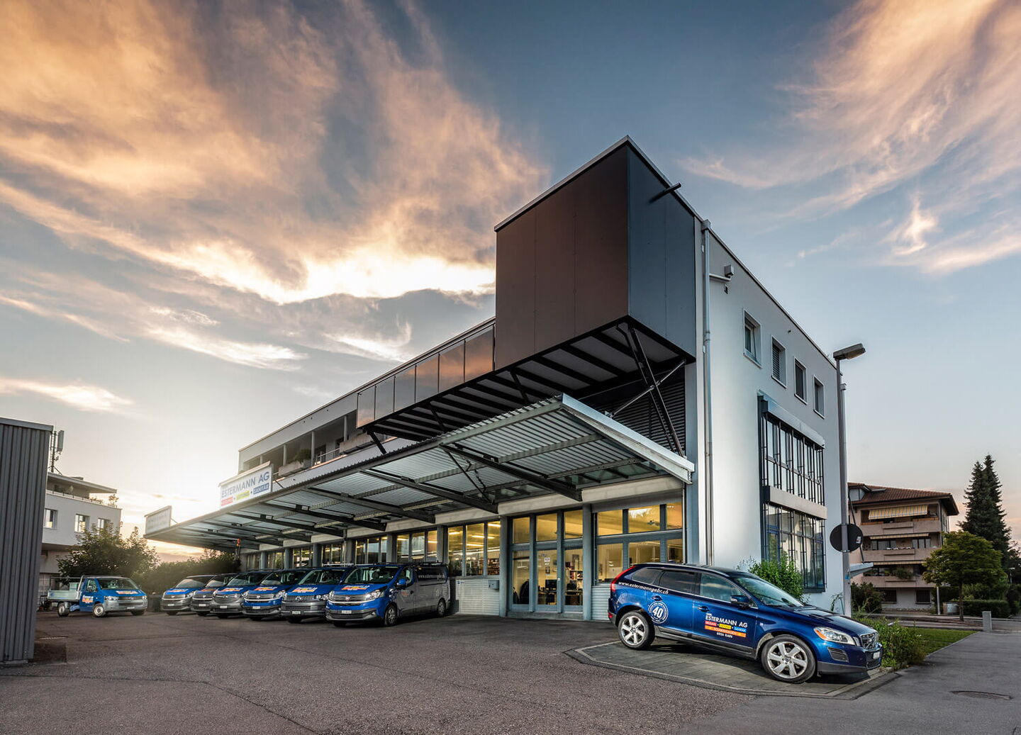 Firmengebäude im Abendsonnenuntergang mit davor geparkten blauen Fahrzeugen