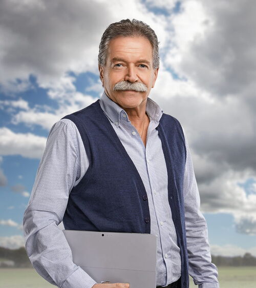 Armin Estermann Handwerker mit Schnauz, Laptop und blauem Overall vor Wiese und Wolkenhimmel