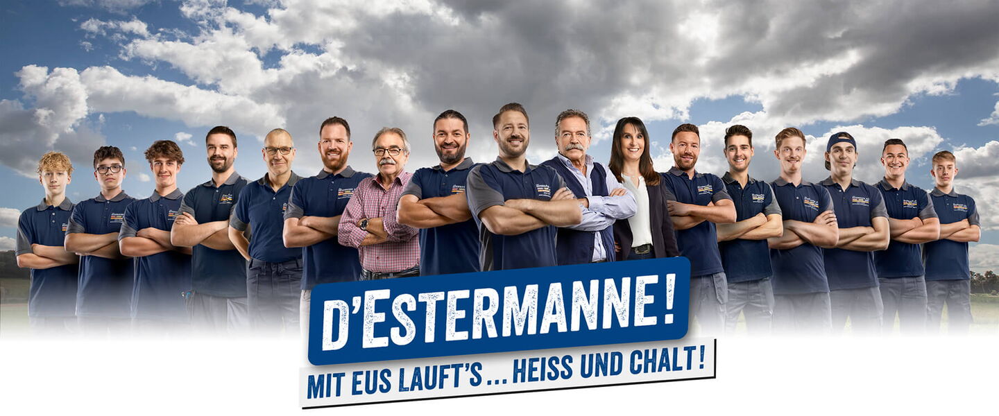 15 Handwerker und eine Frau formiert vor Wiese und Wolkenhimmel