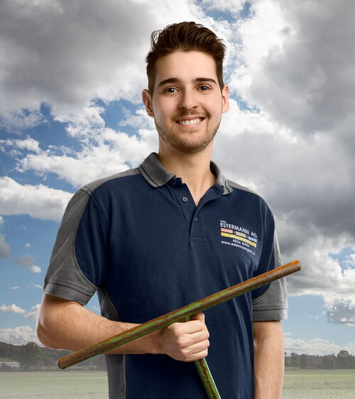 Florian Galliker Handwerker mit blauem Shirt und Drehschlüssel vor Wiese und Wolkenhimmel
