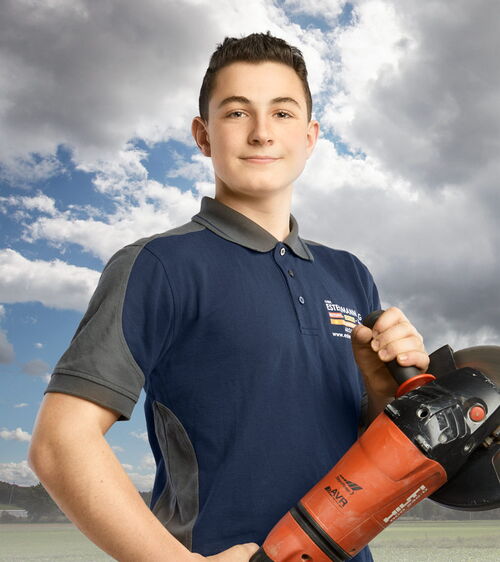 Tom Estermann Handwerker mit blauem Shirt und Winkelschleifer vor Wiese und Wolkenhimmel