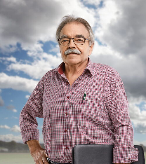 Robert Estermann Handwerker mit Schnauz, kariertem Hemd und Schreibmappe vor Wiese und Wolkenhimmel