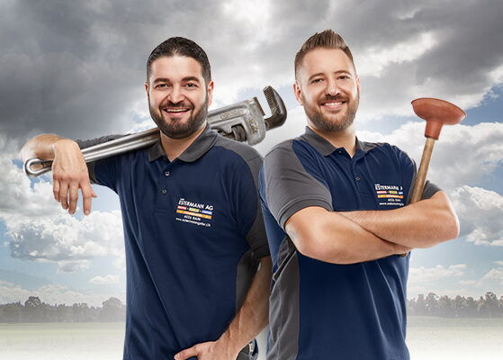 Lars und Armin Estermann sind die Firmeninhaber von Gebr. Estermann AG Zwei Handwerker mit blauem Shirt und Werkzeugen vor Wiese und Wald mit Wolken am blauem Himmel