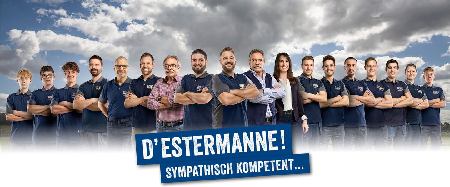 15 Handwerker und eine Frau formiert vor Wiese und Wolkenhimmel