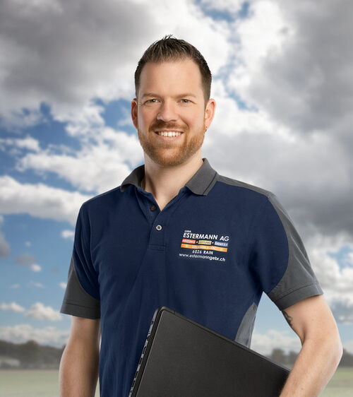 Lukas Brunner Handwerker mit blauem Shirt und Laptop vor Wiese und Wolkenhimmel