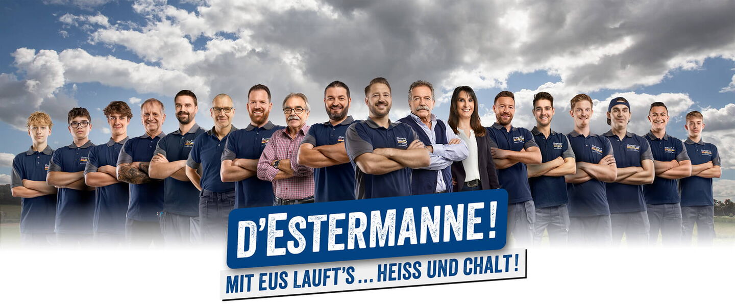 15 Handwerker und eine Frau formiert vor Wiese und Wolkenhimmel
