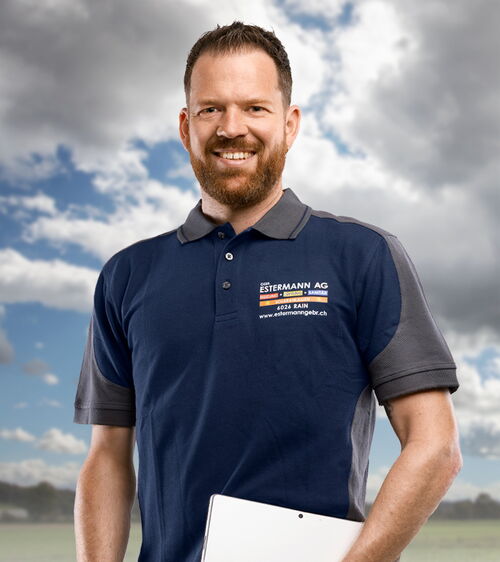 Handwerker mit blauem Shirt und Laptop vor Wiese und Wolkenhimmel