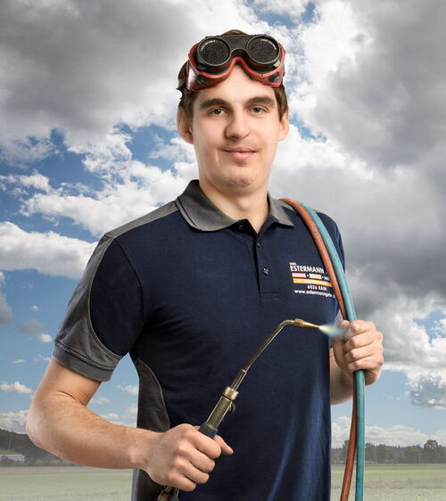 Roman Feer Handwerker mit blauem Shirt und Schweissgerät und Schweissbrille vor Wiese und Wolkenhimmel
