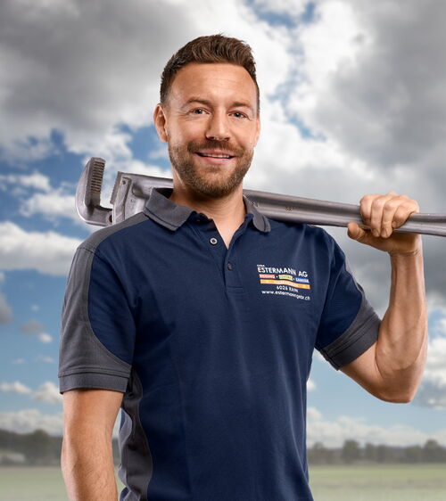 Handwerker mit blauem Shirt und grosser Rohrzange vor Wiese und Wolkenhimmel