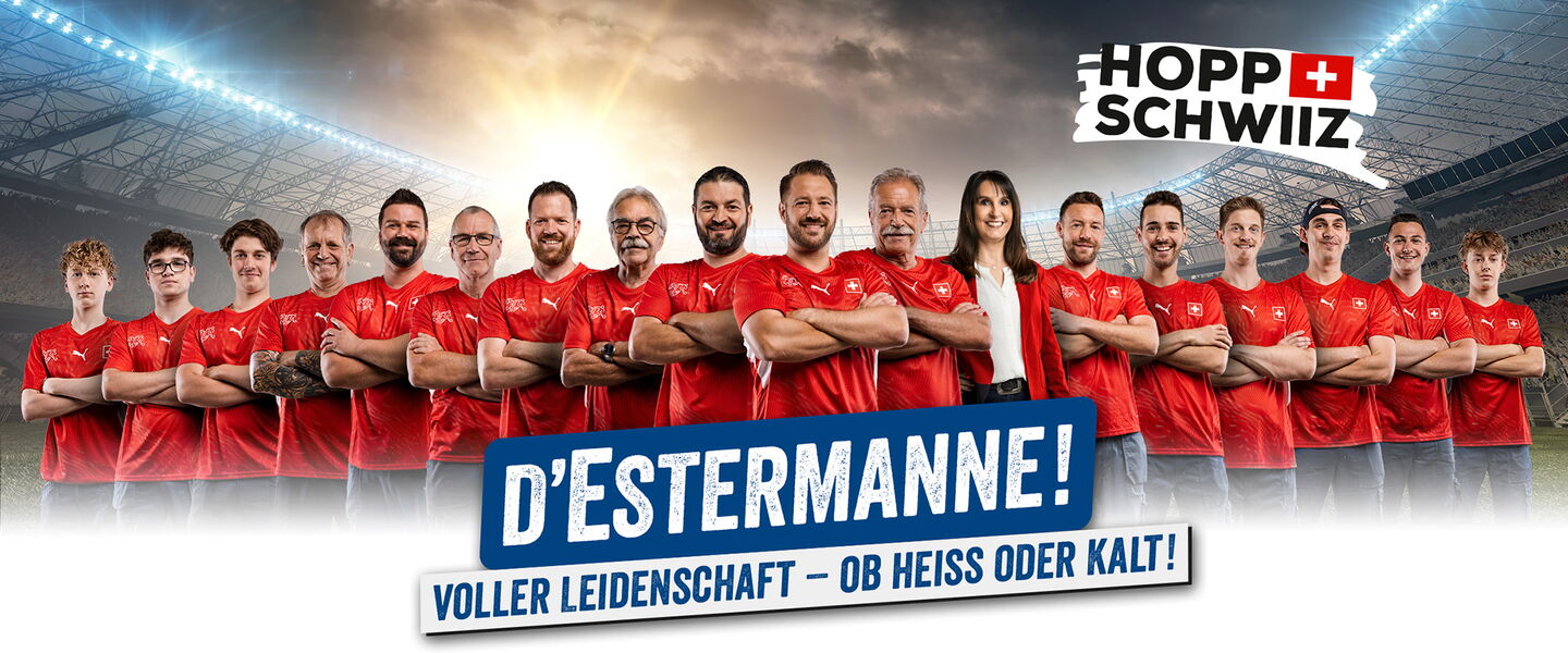 18 Handwerker und eine Frau formiert vor Wiese und Wolkenhimmel mit WM-Schweiz T-Shirt