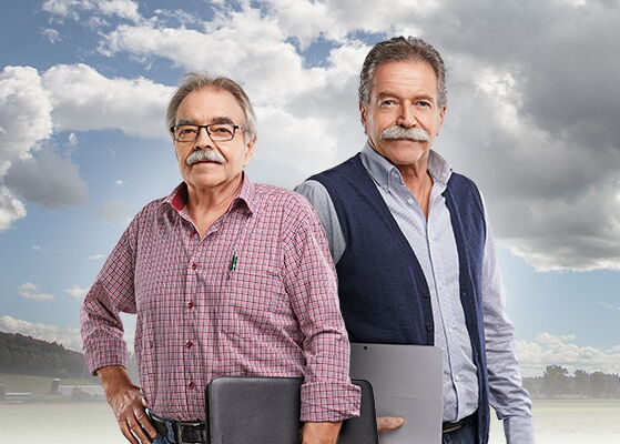 Robert und Armin Estermann, Gründer der Gebr. Estermann AG in Rain Zwei Handwerker mit Laptop und Schreibmappe vor Wiese und Wald mit Wolken am blauem Himmel
