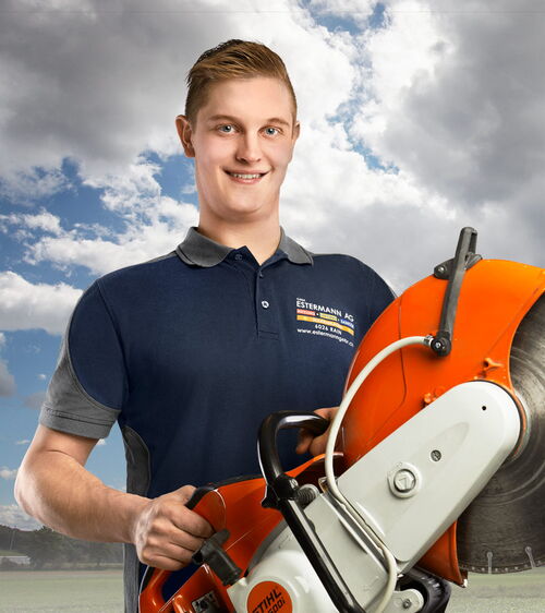 Patrick Wüest, Sanitärinstallateur bei Gebr. Estermann AG Handwerker mit blauem T-Shirt und Trennsäge vor Wolkenhintergrund
